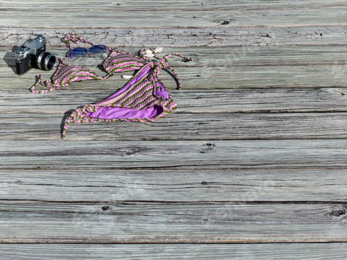 Preview: Bikini On A Weathered Wooden Dock Background With A Vintage Camera, Sunglasses And Seashells.
