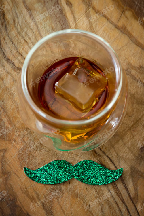 Preview: Close Up Fo A Glass Of Whiskey With A Green Mustache Over A Wooden Background As A Concept For