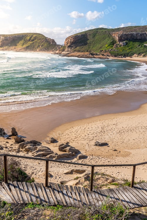 Preview: Portrait Photo Of A Curvy Boardwalk Going Down A Slope With A Huge, Empty Beach And Mountains In