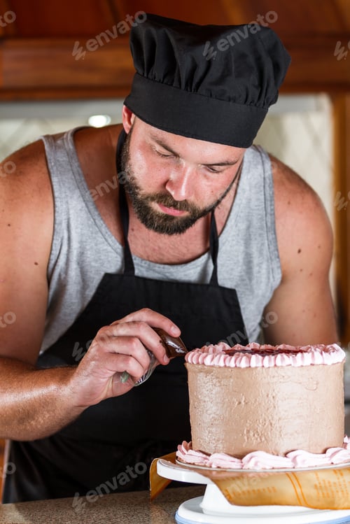 Preview: Male Baker Decorating A Chocolate Birthday Cake With Strawberry Moose Frosting And Dark Chocolate
