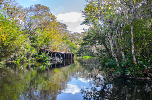 Preview: Scenic Vintage View Of An Old Boathouse On A Florida River Bank As Trees And The Sky Reflect In The