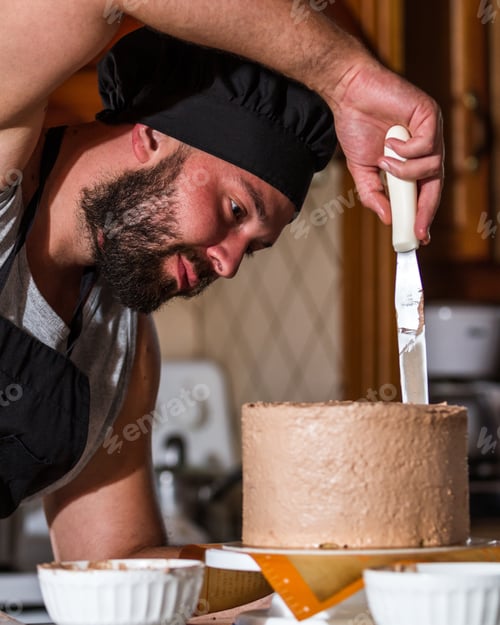 Preview: Male Baker Spreading Chocolate Frosting On A Fresh Baked Birthday Cake