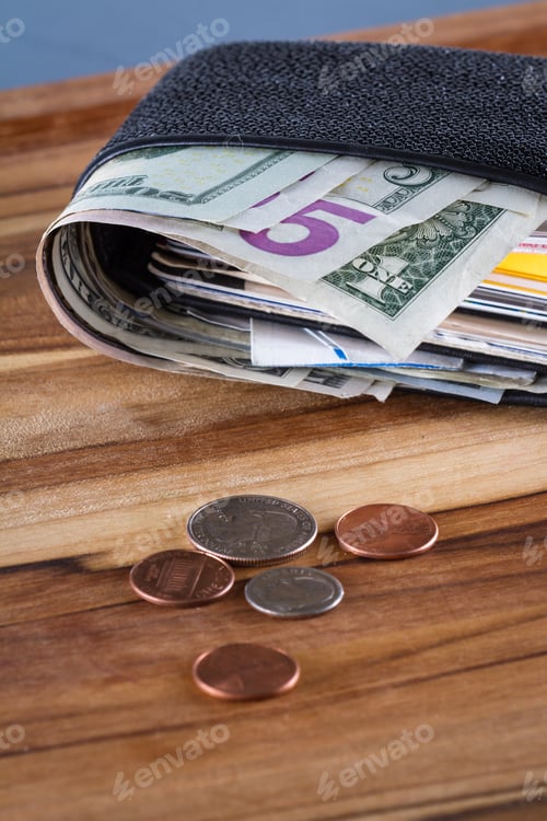 Preview: Close Up Of A Wallet With American Dollars Sticking Out And Change On A Wooden Table