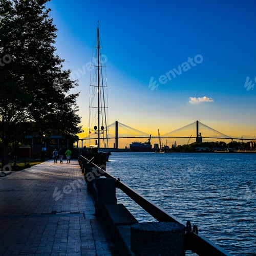 Preview: The Bridge Over The Savannah River From The Riverwalk With Tourists Walking And A Sailboat Docked