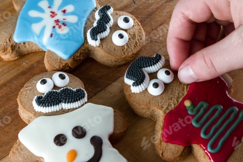 Preview: Close Up Of Funny Gingerbread Cookies On A Wooden Table With Young Hands Placing Decorations And