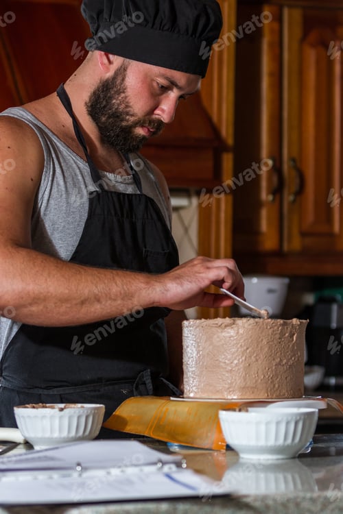 Preview: Male Baker Spreading Chocolate Frosting On A Fresh Baked Birthday Cake