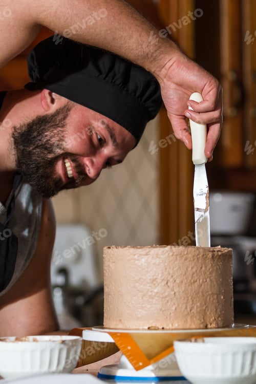 Preview: Male Baker Spreading Chocolate Frosting On A Fresh Baked Birthday Cake