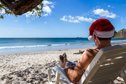 Preview: Holiday Concept With A Man Wearing A Santa Hat Relaxing On A Lounge Chair At The Beach In Costa Rica