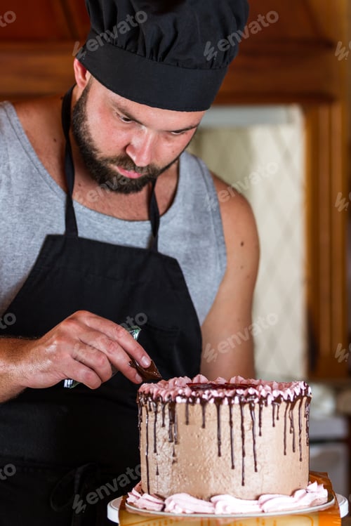 Preview: Male Baker Decorating A Chocolate Birthday Cake With Strawberry Moose Frosting And Dark Chocolate