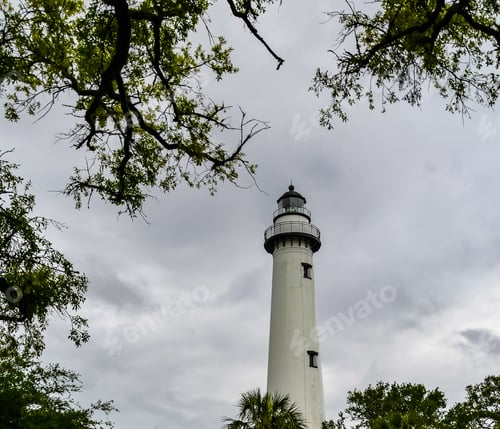 Preview: The St. Simons Island Lighthouse Against A Cloudy Evening Sky With Tree Branches Framing The Tower