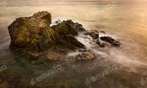 Preview: Slow Exposure Blurs The Waves In The Ocean As They Break Over A Rocky Outcrop At Sunset