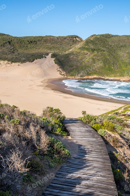Preview: Portrait Photo Of A Curvy Boardwalk Going Down A Slope With A Huge, Empty Beach And Mountains In