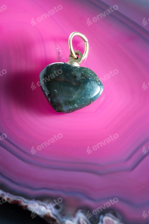 Preview: Close Up Of A Polished Green Stone Cut Into The Shape Of A Heart On A Pink Tone Background