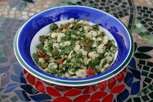 Preview: Closeup Of Salad With White Beans And Herbs On A Plate With Blue And Green Rim On A Table With A
