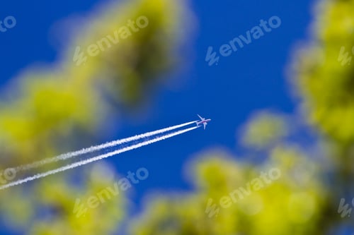 Preview: High Flying Plane On A Blue Sky With Vapor Or Chemtrail And Green Spring Trees Out Of Focus