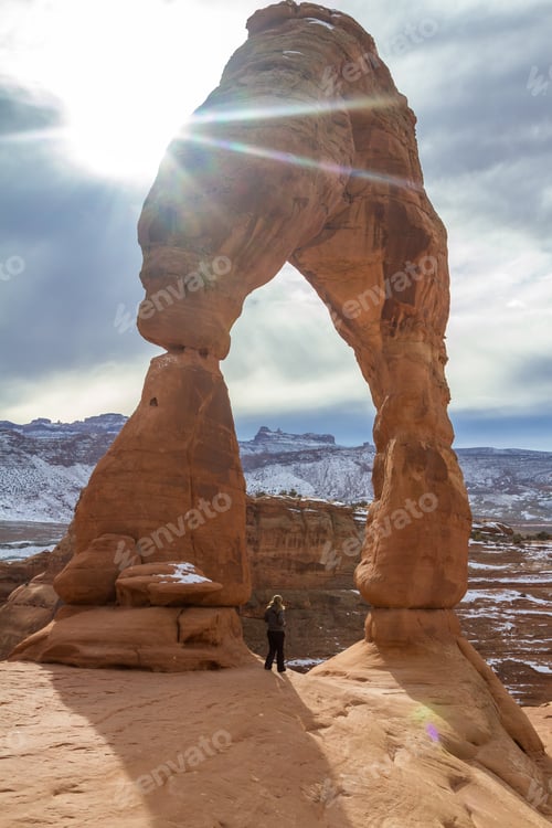 Preview: Delicate Arch In The Winter With A Hiker Standing At The Base Of To Show A Size Perspective Of This