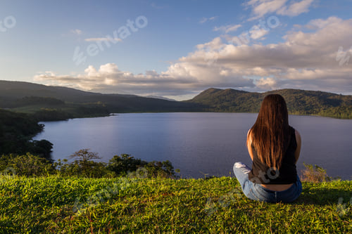 Preview: Young Woman Sitting At The Top Of A Hill Overlooking Cote Lake Taking In The Serene And Natural