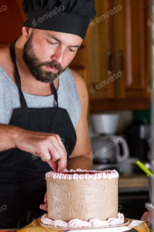 Preview: Male Baker Decorating A Chocolate Birthday Cake With Strawberry Moose Frosting