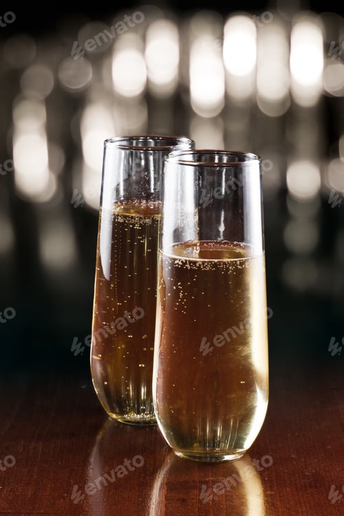 Preview: Two Champagne Flutes On A Bar Top With A Busy Out Of Focus Background