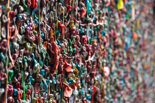 Vista previa: Foto de primer plano de cientos de coloridos trozos de goma de mascar pegados en una pared de un callejón. Disparado