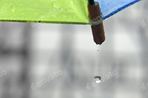 Preview: Raindrop Falling Off A Blue And Green Umbrella With A Blurred Half-Timbered Facade In The Background