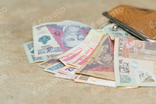 Preview: Colorful Bills From Guatemala And Belize Spilling Out Of A Leather Bag On A Counter Top
