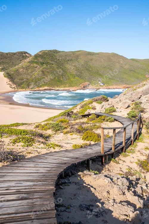 Preview: Portrait Photo Of A Curvy Boardwalk Going Down A Slope With A Huge, Empty Beach And Mountains In