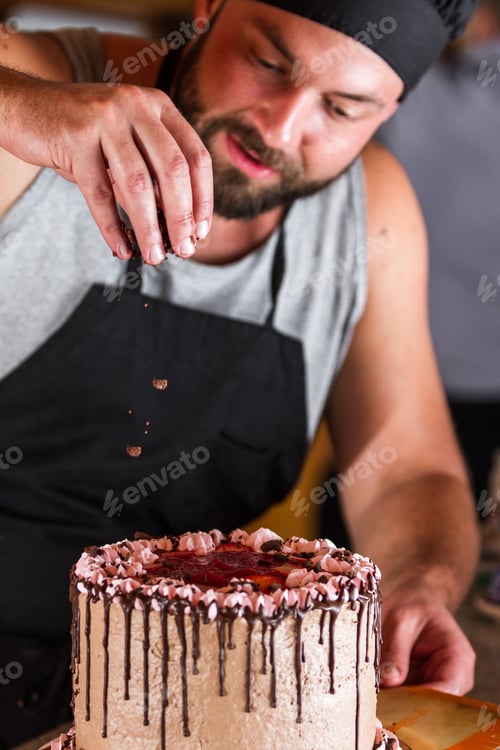 Preview: Male Baker Decorating A Chocolate Birthday Cake With Strawberry Moose Frosting And Dark Chocolate