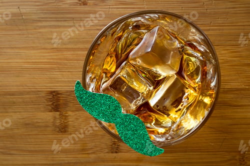 Preview: Close Up Fo A Glass Of Whiskey With A Green Mustache Over A Wooden Background As A Concept For