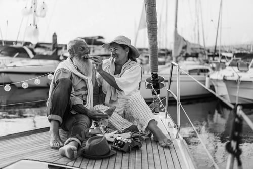 Preview: Senior Couple Having Fun Eating Fruits On Sail Boat - Focus On Woman Face - Black And White Editing