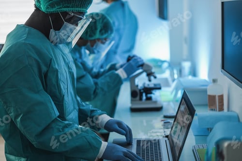 Preview: Medical Workers In Hazmat Suit Working With Computer And Micoroscope Inside Hospital Lab During