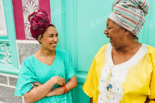 Preview: Happy African Mother And Her Daughter Wearing Afro Clothes While Talking In Front Of Their House