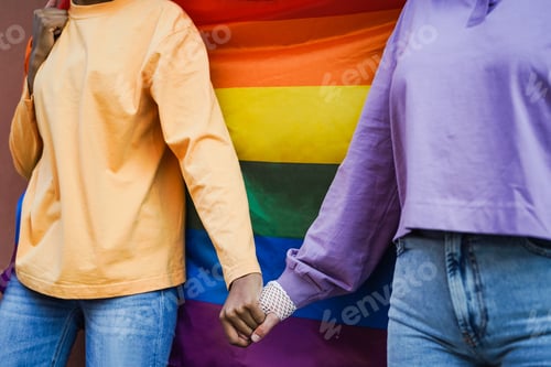 Preview: Happy Women Gay Couple Holding Hands With Rainbow Flag On Background - Soft Focus On Hands