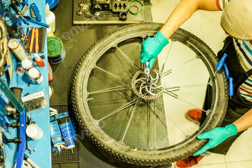 Preview: Top View Of Stylish Bicycle Mechanic Working In Mountain Bike Shop - Young Man Checking Wheel Spoke