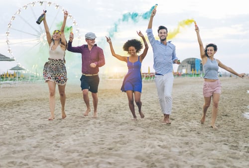 Preview: Young Friends Running With Smoke Bombs Champagne Bottle On The Beach At Sunset - Happy People