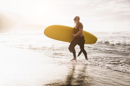 Preview: Senior Surfer Man Walking On The Beach After Surf Session At Summer Sunset - Focus On Face