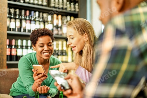 Preview: Portrait Of Cheerful Young Friends Looking At Smart Phones While Sitting In Pub Wine Bar - Mixed