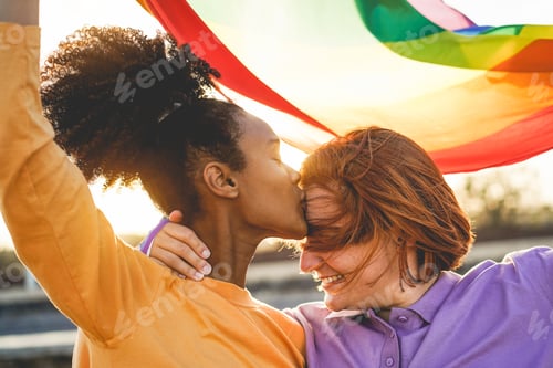 Preview: Happy Women Gay Couple Having Tender Moment Holding Rainbow Flag Outdoor - Main Focus On African