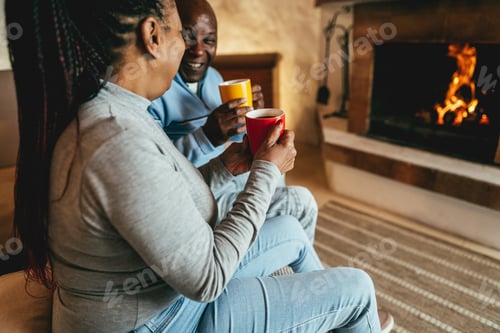 Preview: African Couple Drinking Hot Chocolate In Front Of Cozy Fireplace At Home - Winter Lifestyle Concept