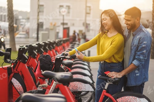 Preview: Young People Renting Electric Bicycle With Smartphone App - Happy Couple Having Fun With New Trends