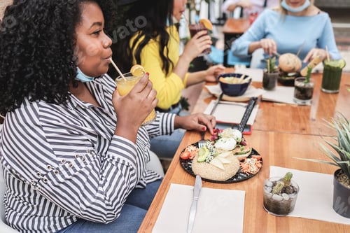 Preview: Young Multiracial Friends Having Breakfast In Restaurant Outdoors With Masks Under Chins - Focus On