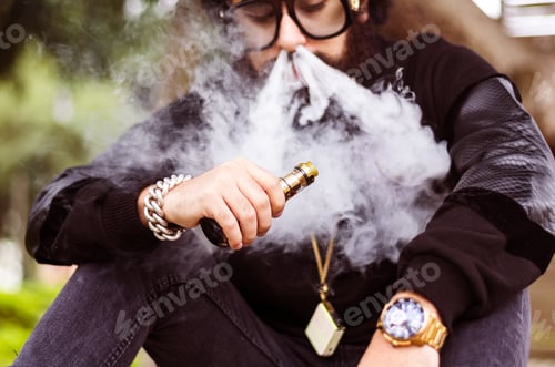 Preview: Man With A Beard Smokes An Electronic Cigarette Sit On A Bench In The Park