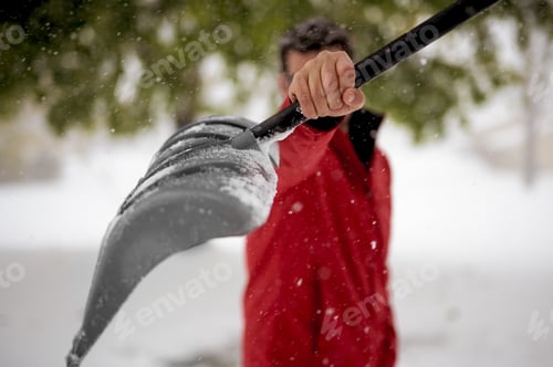 Preview: A Closeup Shot Of A Male Holding Up The Snow Shovel Towards The Camera With A Blurred Background