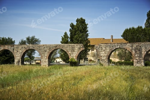Preview: An Old Arch Bridge On A Grass Field With Trees And A Building In The Background