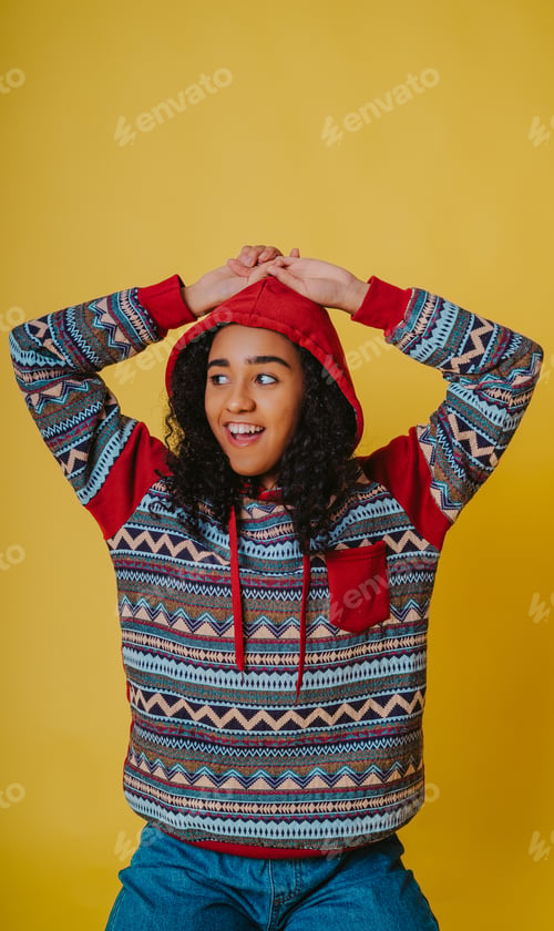Preview: A Portrait Of A Cheerful Hispanic Female With Curly Hair Wearing A Hoodie And Jeans Against A