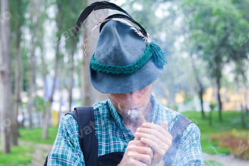 Preview: Young Caucasian Man Wearing Traditional German Clothes Smokes Cigar In The Summer Park.