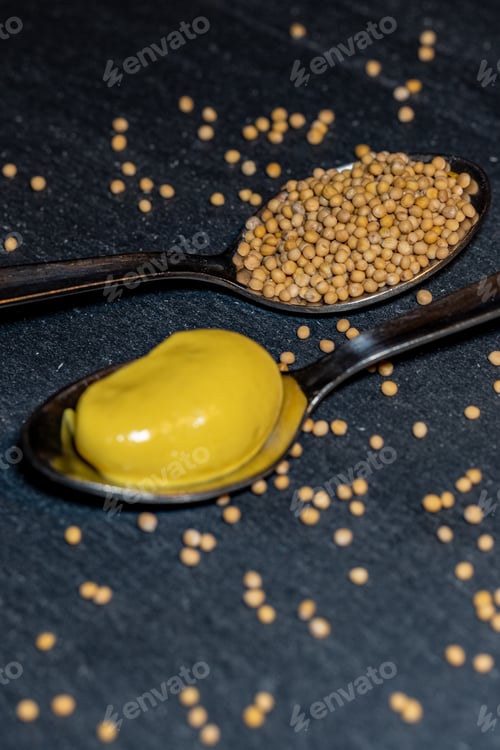 Preview: Two Spoons With Mustard And Mustard Seeds Lie On A Black Stone Table They Are Surrounded By More