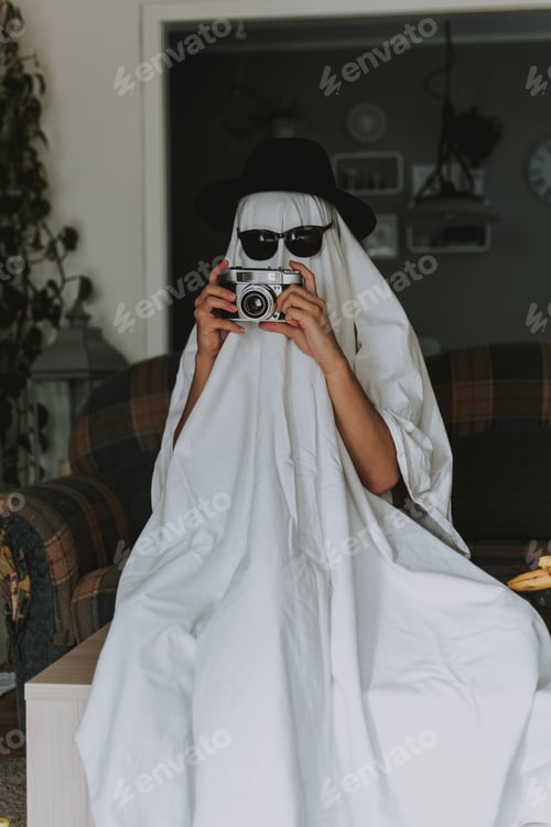 Preview: A Person Wearing A White Bedsheet Over His Head Like A Ghost And Holding A Camera In His Hands