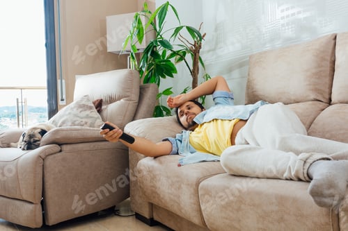 Preview: A Photo Of A Handsome Hispanic Man Lying On A Sofa And Watching Tv