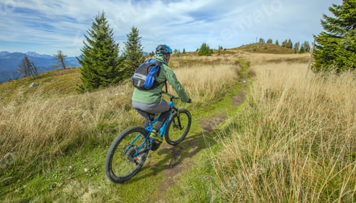 Preview: A Beautiful Shot Of A Male Cyclist Passing Through A Grassy Field With Some Trees On A Windy Day